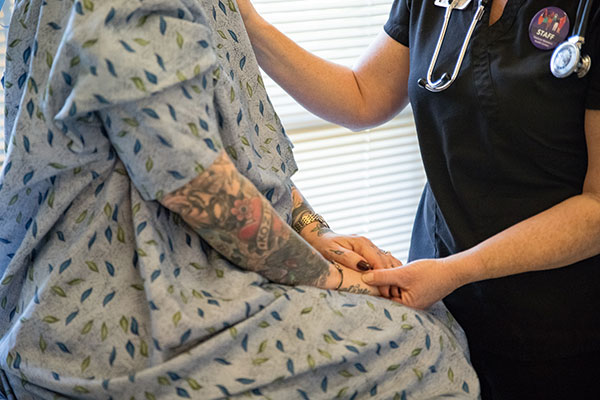 A close-up image of a staffer holding the hand of a model posing as a patient.
