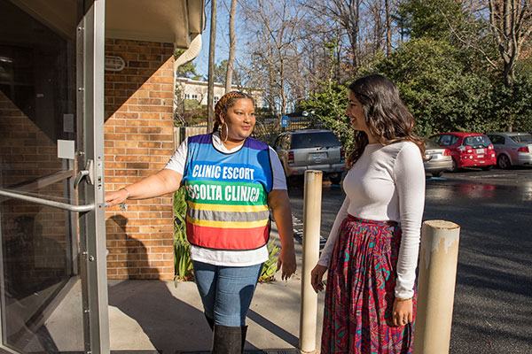 A clinic escort holds the door open for a model posing as a patient