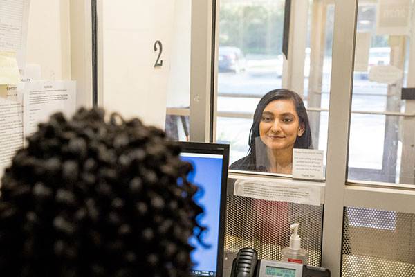A model poses as a patient speaking with a staff member at the front desk.