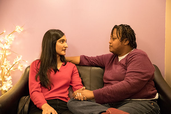 Two models hold hands while sitting on a couch.
