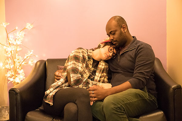 Models sit on a black leather couch inside the clinic, the model on the right poses as if they are comforting the model on the left.