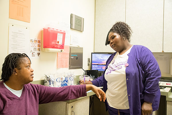 A model poses as a patient speaking with a clinic staffer.
