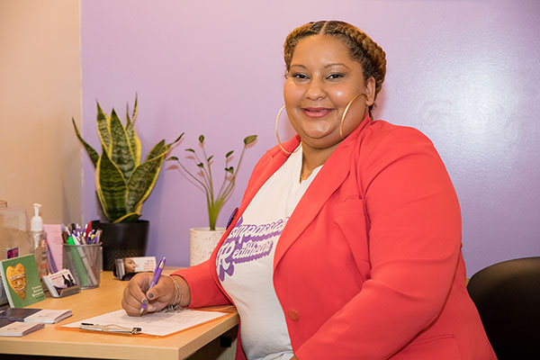 A clinic staffer smiles at the camera while sitting at a desk.