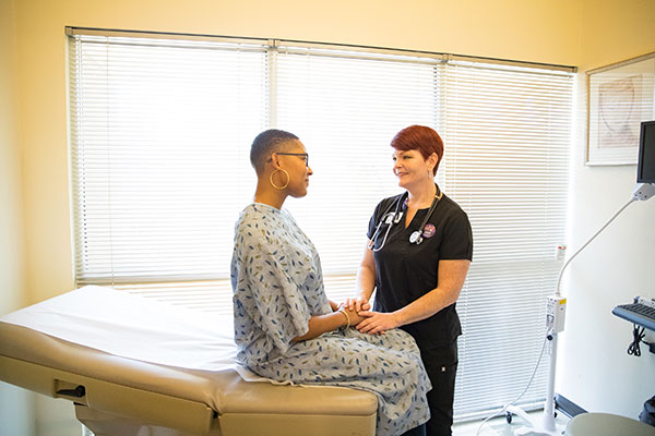 A clinic staffer speaks with a model posing as a patient in a procedure room.