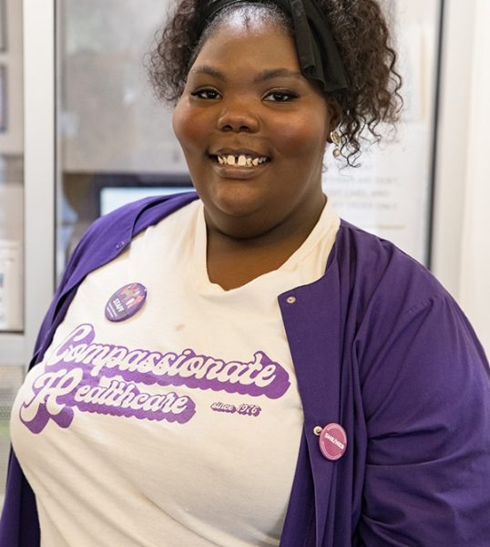 Clinic staff member smiles in a Feminist Women’s Health Center t-shirt.