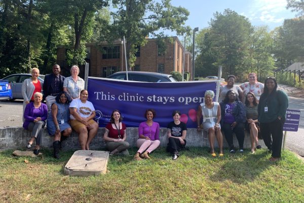 Staff members and volunteers pose in front of the Feminist Women’s Health Center with a banner that reads “This clinic stays open.”