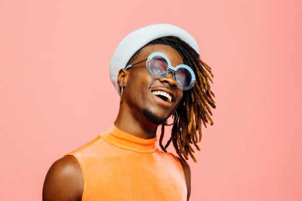 Portrait of a happy young man with sunglasses and cap laughing, isolated on pink.